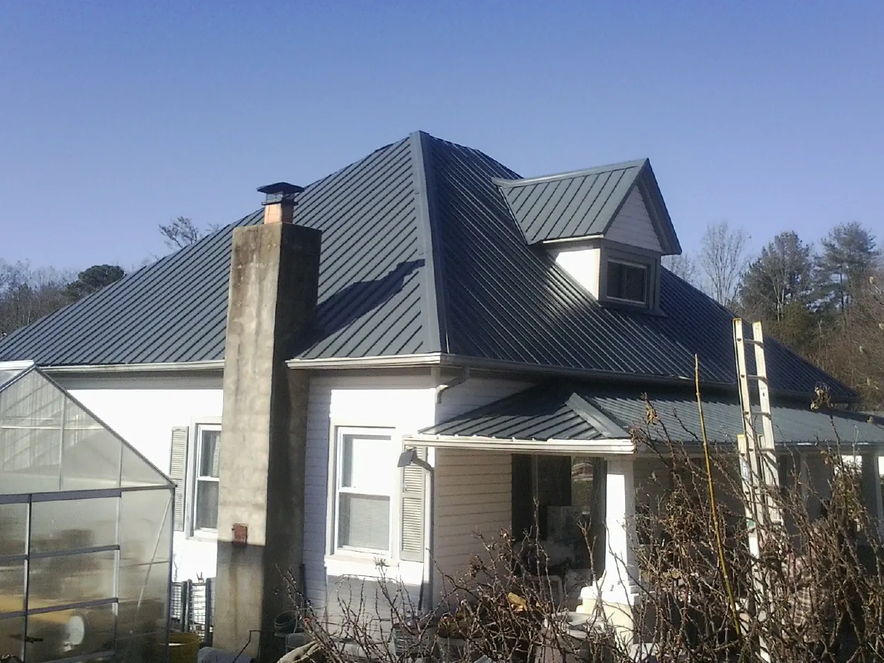 Dark blue standing seam metal roof on a white farmhouse with dormer — Slate & Tile Roof Repair by Roofing Brothers in Honeoye