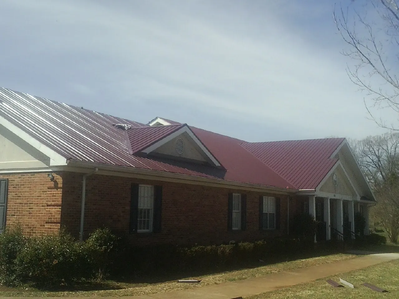 Red metal roof with gabled entries on a long brick building, from a Hail Damage Roof Repair job in Honeoye