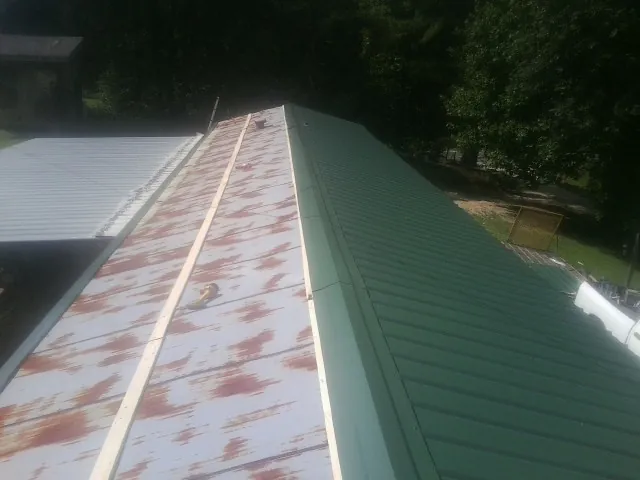 Old rusted panels beside newly installed green metal roofing — Wind Damage Roof Repair by Roofing Brothers in Honeoye