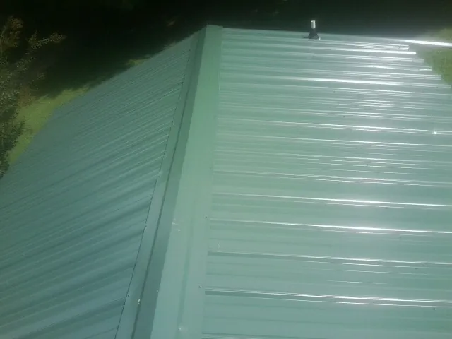 New green metal panels meeting at the ridge of a roof — Flat Roof Repair work by our crew in Honeoye