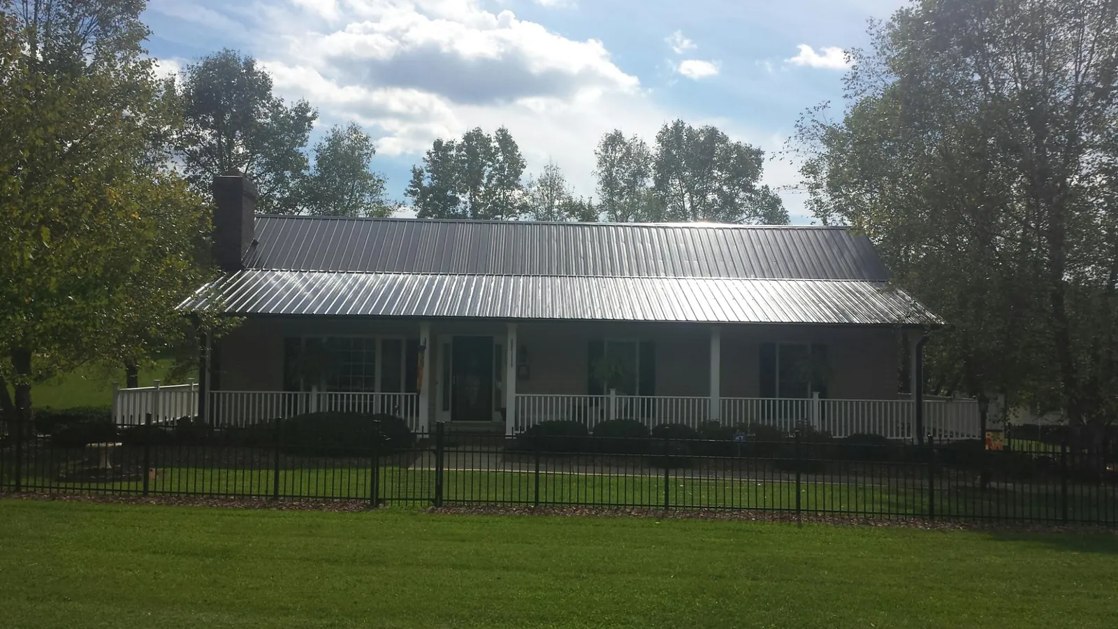 Gray metal roof on a brick ranch with a full width front porch — Gutter Guard Installation work by our crew in Honeoye