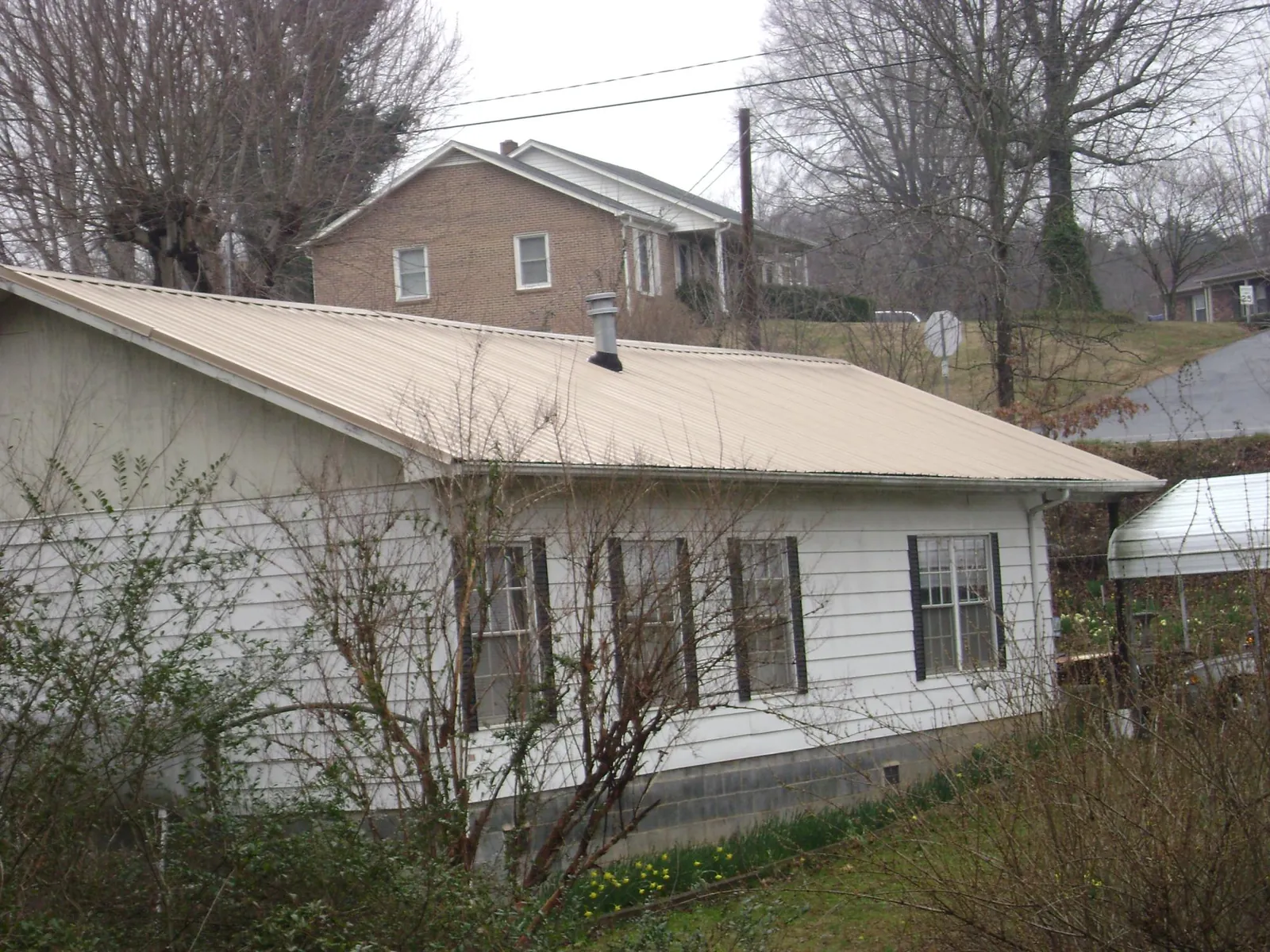 Tan metal roof on a white sided house set into a hillside — Commercial Roofing by Roofing Brothers in Honeoye