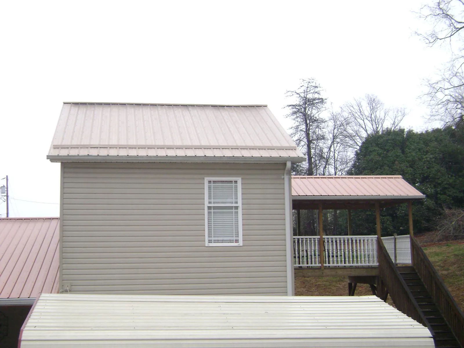 Tan metal roofs on a two story addition and attached porch, from a Roof Replacement job in Honeoye